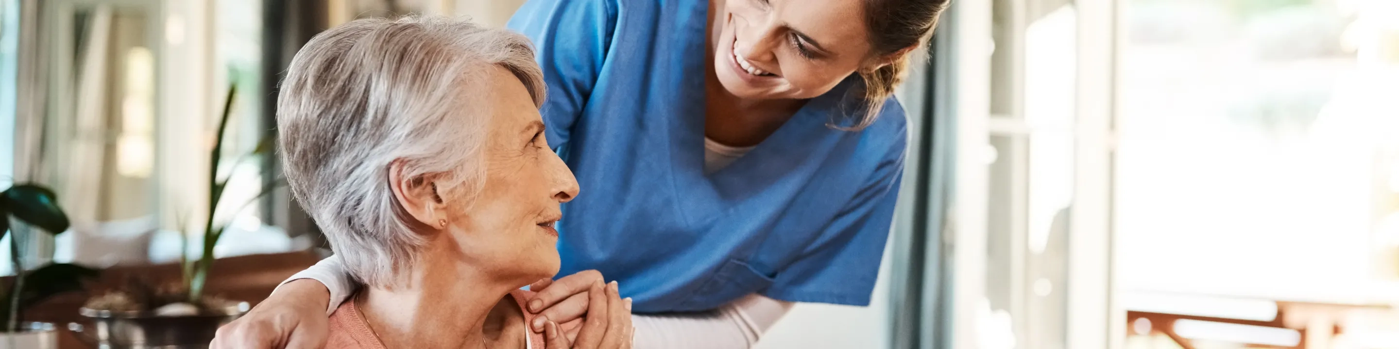 Senior woman with physical therapist hugging at home. Banner for design.